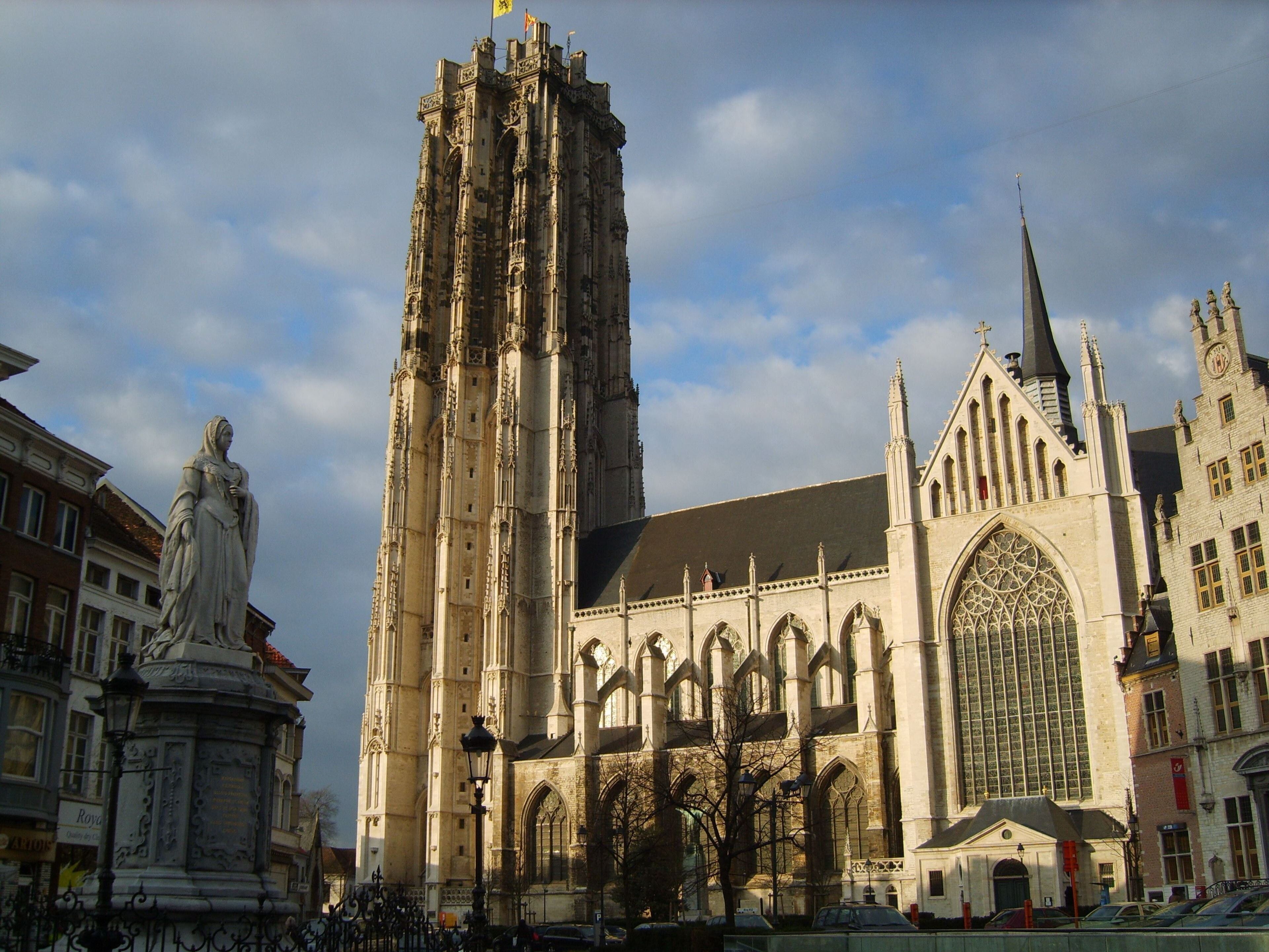 Een historisch kathedraal met een hoge spits, een groot roosvenster en een standbeeld ervoor.