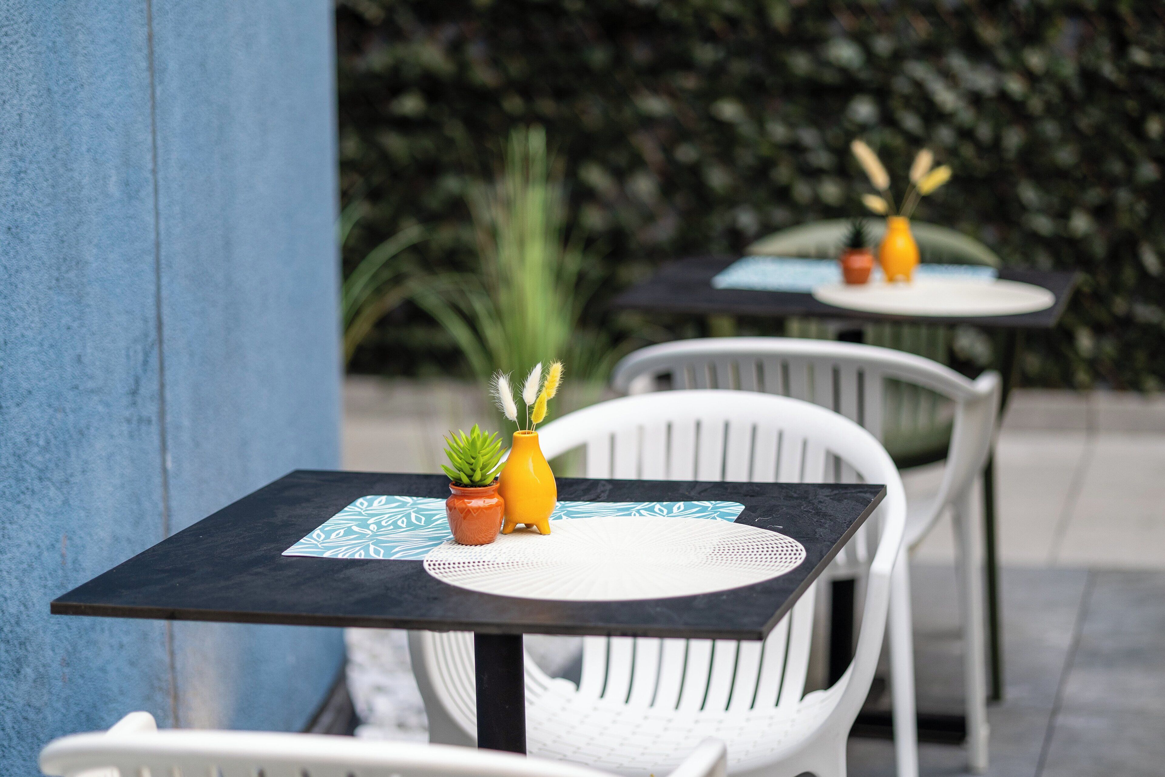 Two outdoor tables with white chairs, each with a small potted plant and a yellow vase.