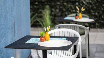 Two outdoor tables with white chairs, each with a small potted plant and a yellow vase.