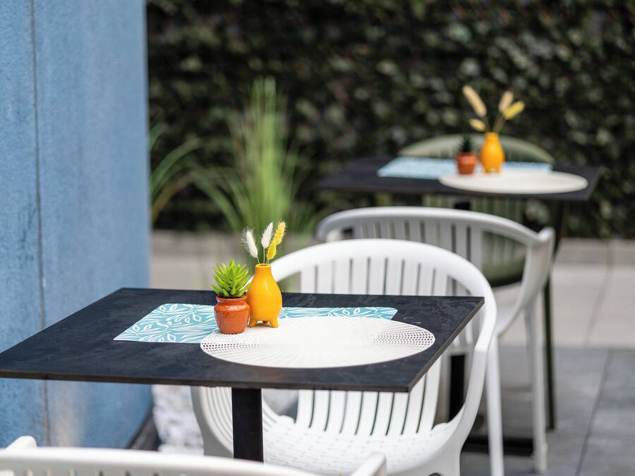 Two outdoor tables with white chairs, each with a small potted plant and a yellow vase.
