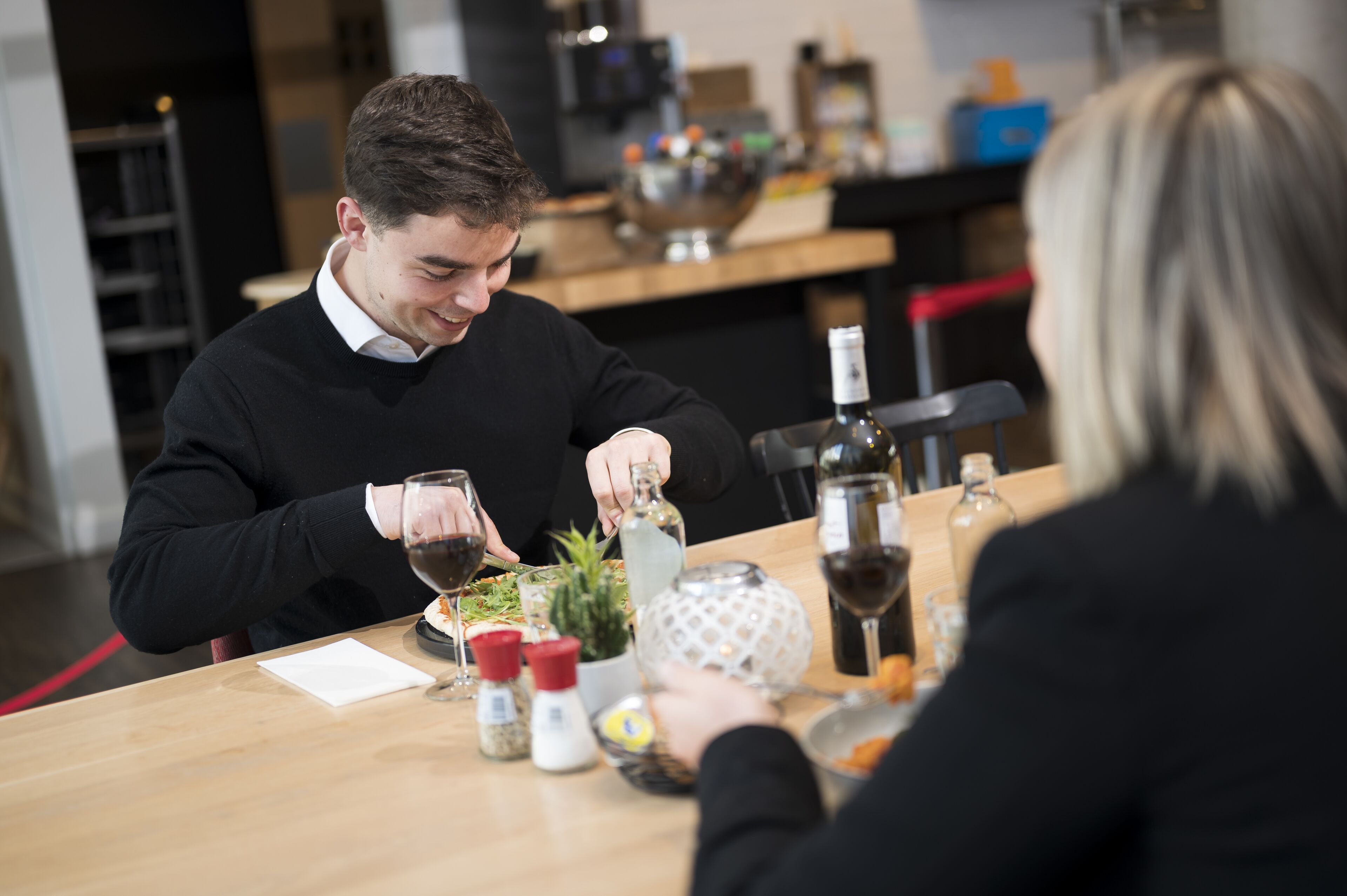 A dining table with a bottle of wine, a bowl, and some condiments.