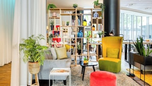 Una sala moderna con un sofá, un pouf rojo, una estantería y un sillón amarillo.