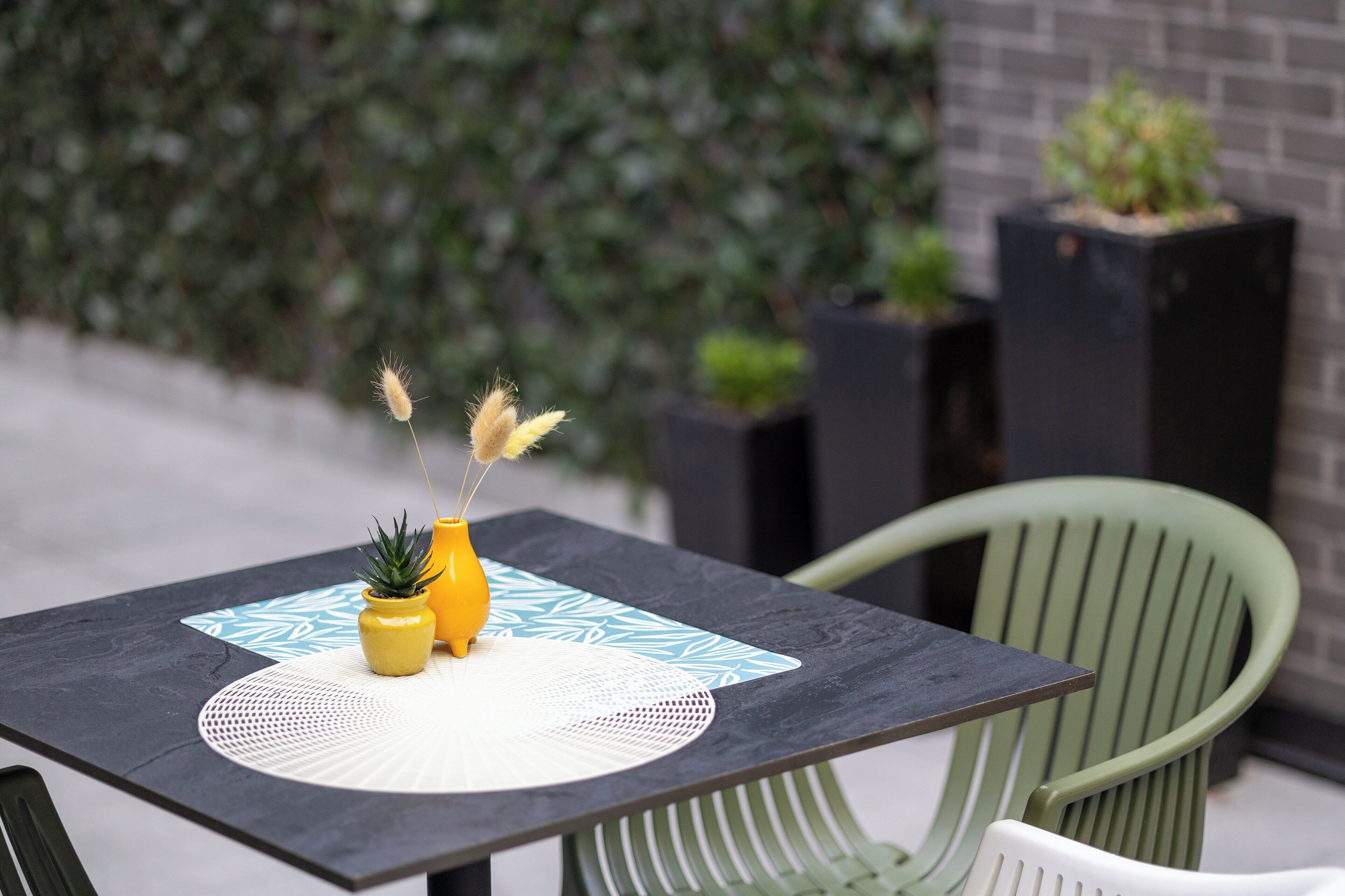 A table with a patterned placemat, a yellow vase with a plant, and a decorative feather.