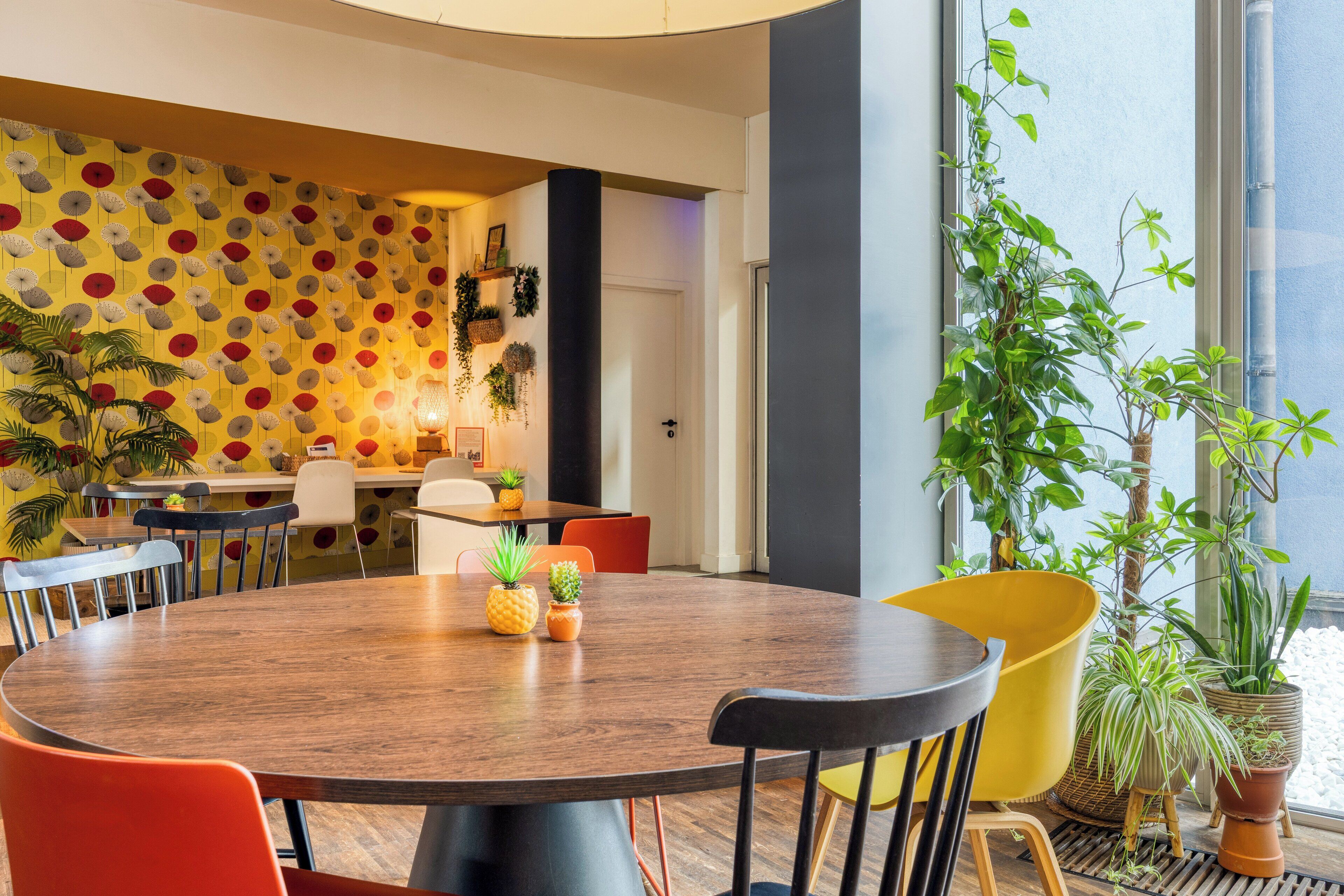 Een moderne eetruimte met een ronde houten tafel, kleurrijke stoelen en potplanten.