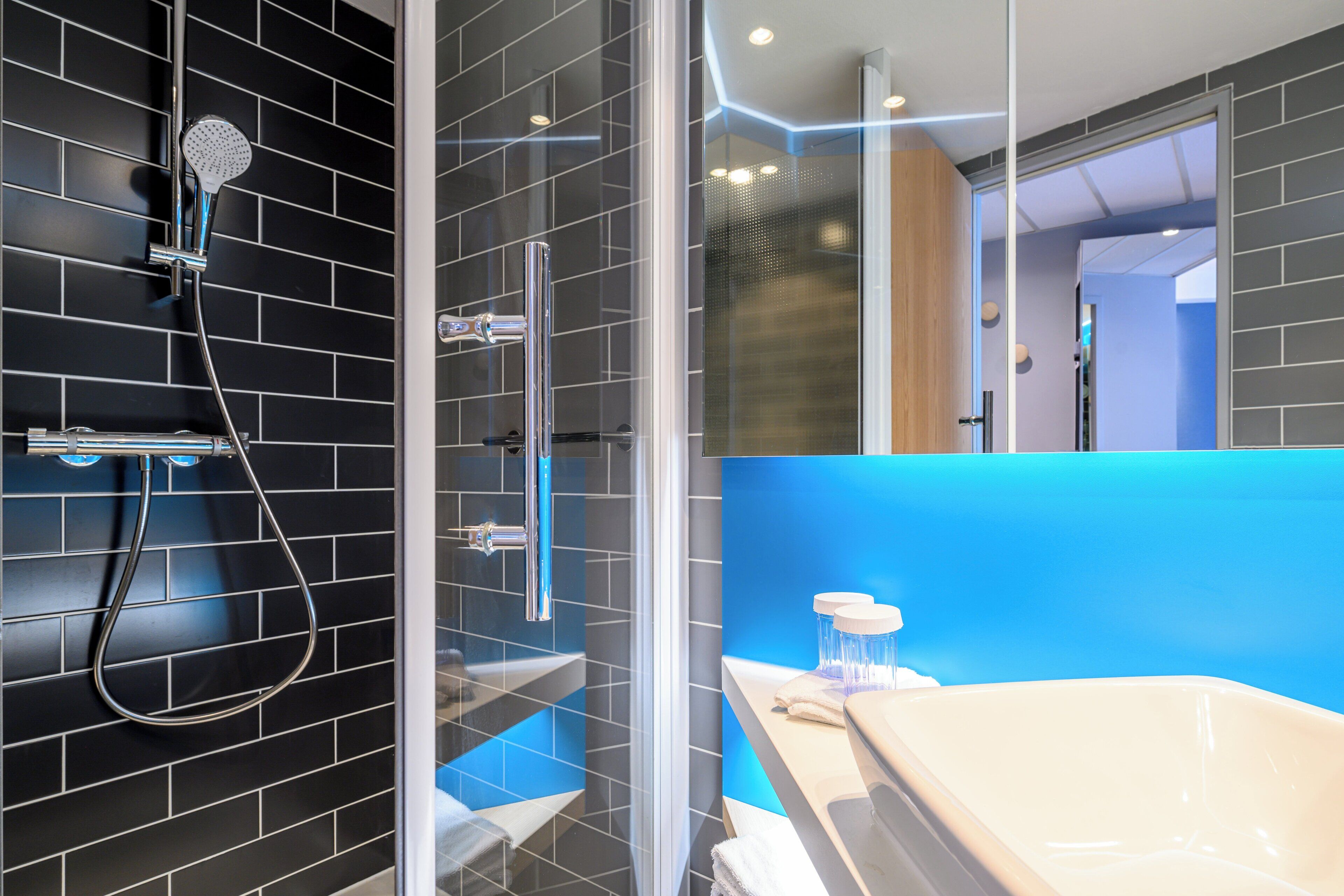 Une salle de bain moderne avec une douche à parois de verre, une baignoire blanche et un mur d’accent bleu.
