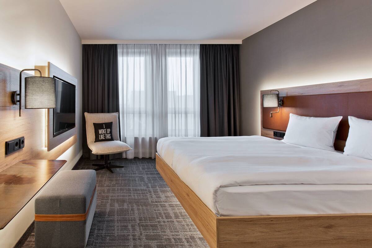 Une chambre d’hôtel avec un grand lit, un bureau avec une télévision, une chaise et une vue sur l’extérieur par la fenêtre.