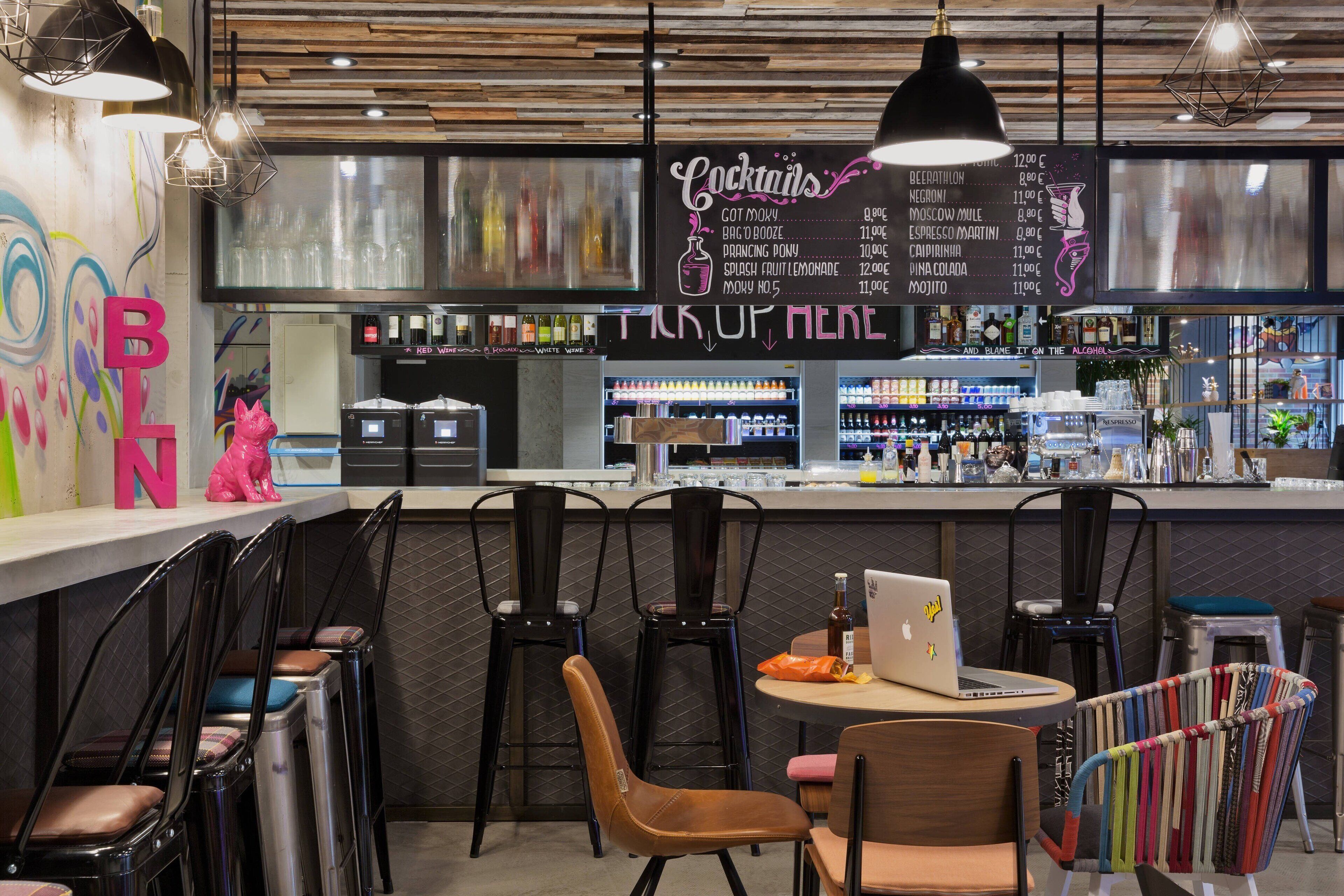 A bar area with a menu board, bar stools, and a laptop on a table.