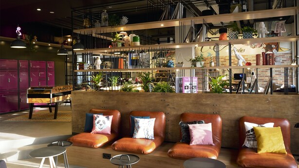 Een moderne lounge met lederen zitplaatsen, een piano en diverse decoratieve items op planken.