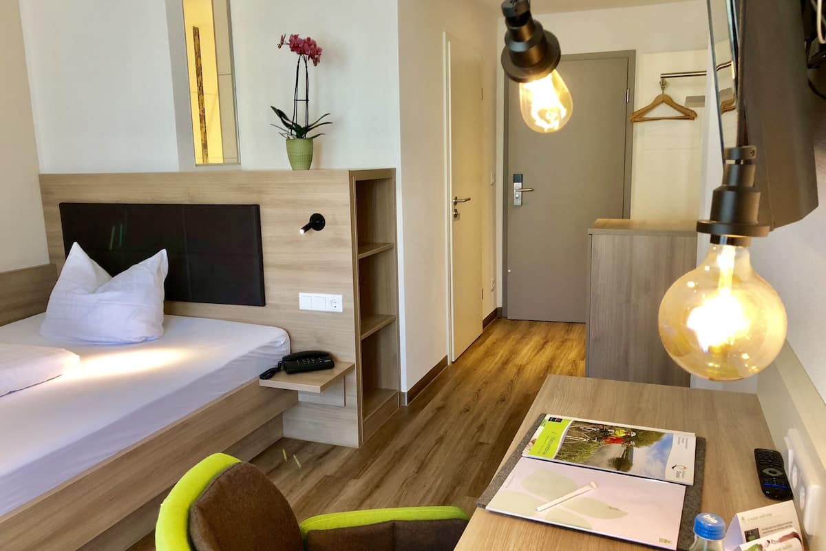 Une chambre d’hôtel comprenant un lit, une table de chevet, une lampe et un petit bureau avec une chaise.