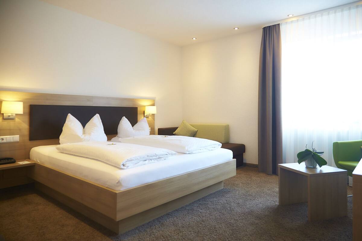 Une chambre d’hôtel avec un grand lit, des lampes de chevet, une petite table et une chaise verte.