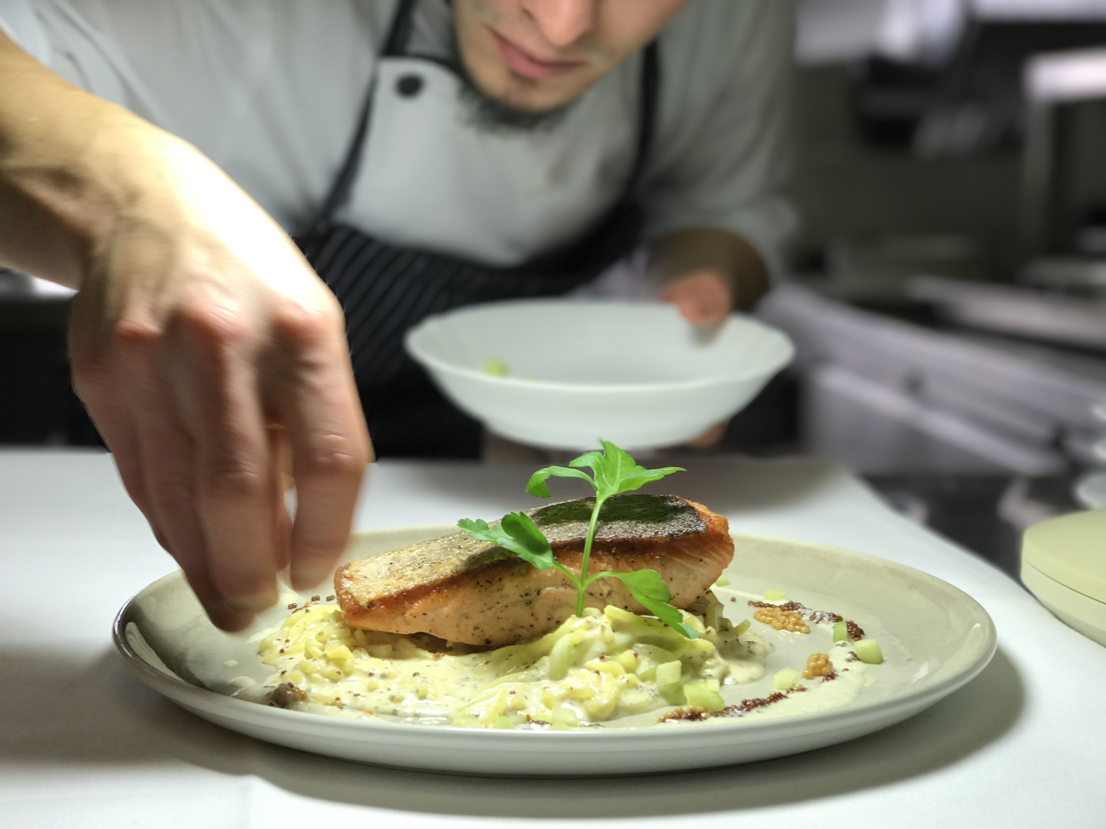 A chef placing a fish on a plate with a garnish.