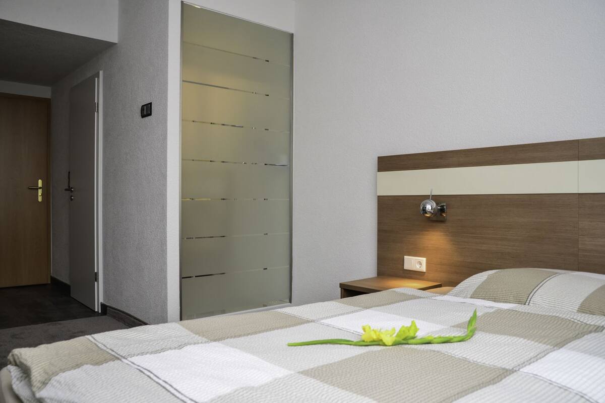 Une chambre d’hôtel comprenant un lit, une table de chevet, une commode, une lampe fixée au mur et une armoire avec des portes coulissantes.