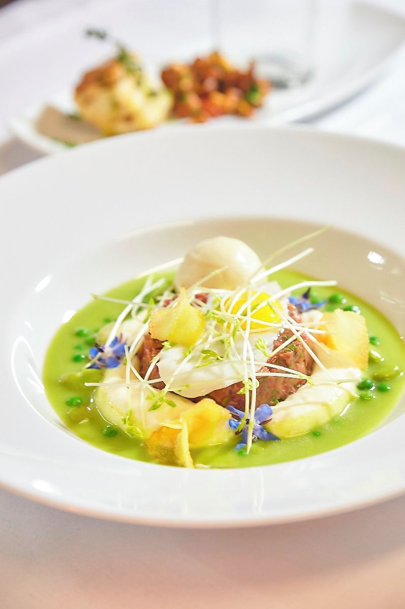 Un plato blanco con salsa verde, una esfera blanca y guarniciones.