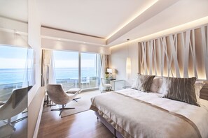 Habitación de hotel moderna con una cama grande, un escritorio y una silla. Se ve el océano a través de amplias ventanas.