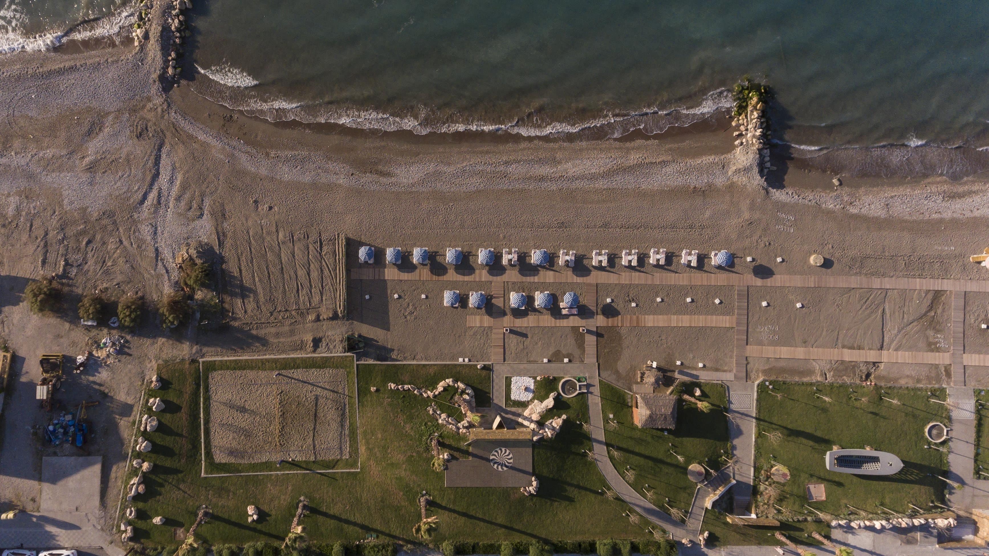 An aerial view of a beachside resort with rows of beach umbrellas, a pool area, and a boardwalk.