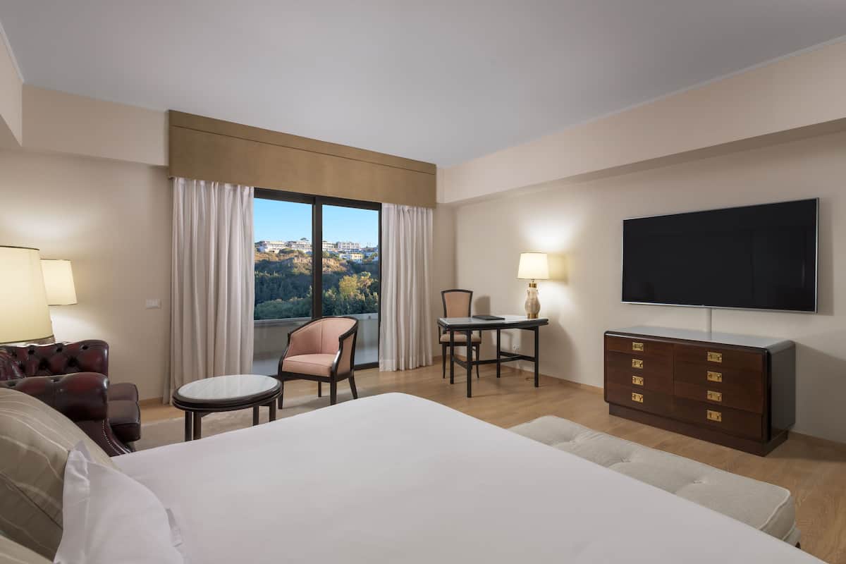 A hotel room with a large bed, a TV, a desk with a chair, a small table, and a sofa.