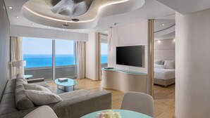 A modern living room with a sofa, a glass table with a vase, a flat-screen TV, and a balcony with a view of the sea. - Rodos Palace Hotel (Rhodes)