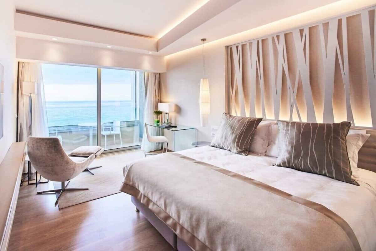 A modern hotel room with a large bed, a desk, a chair, and a view of the ocean.