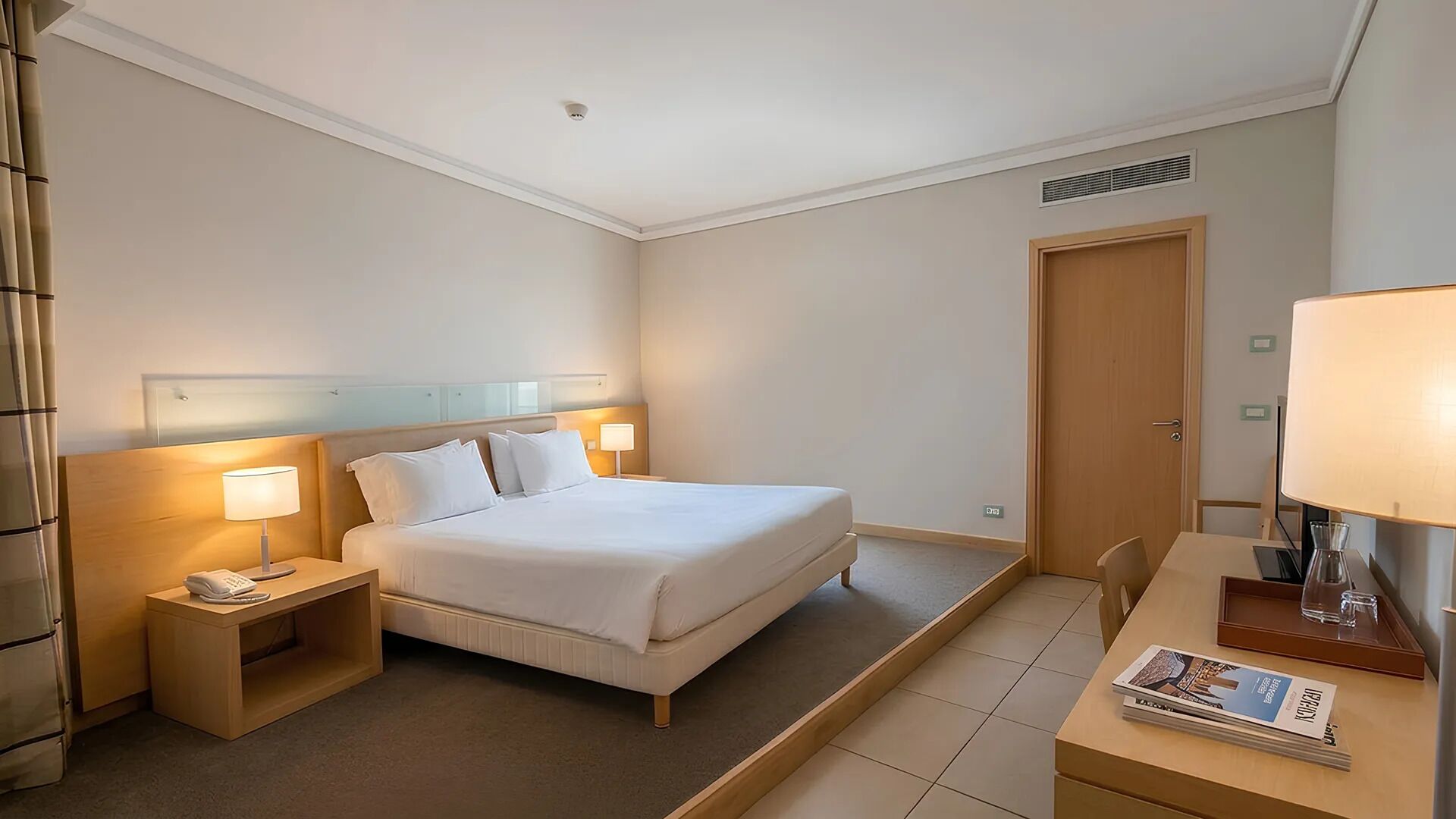 A hotel room with a bed, bedside tables, a desk, and a chair.