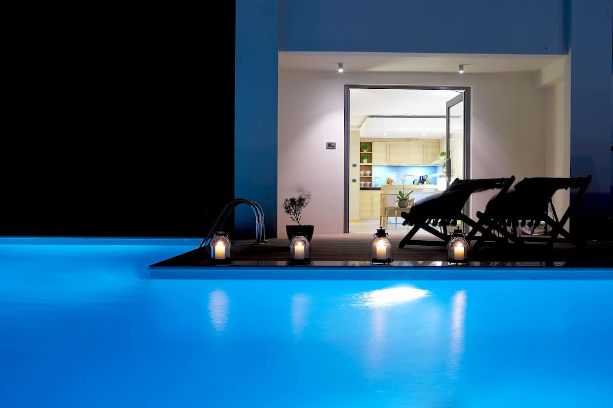 A swimming pool area with lounge chairs and candles, leading to a well-lit kitchen area.