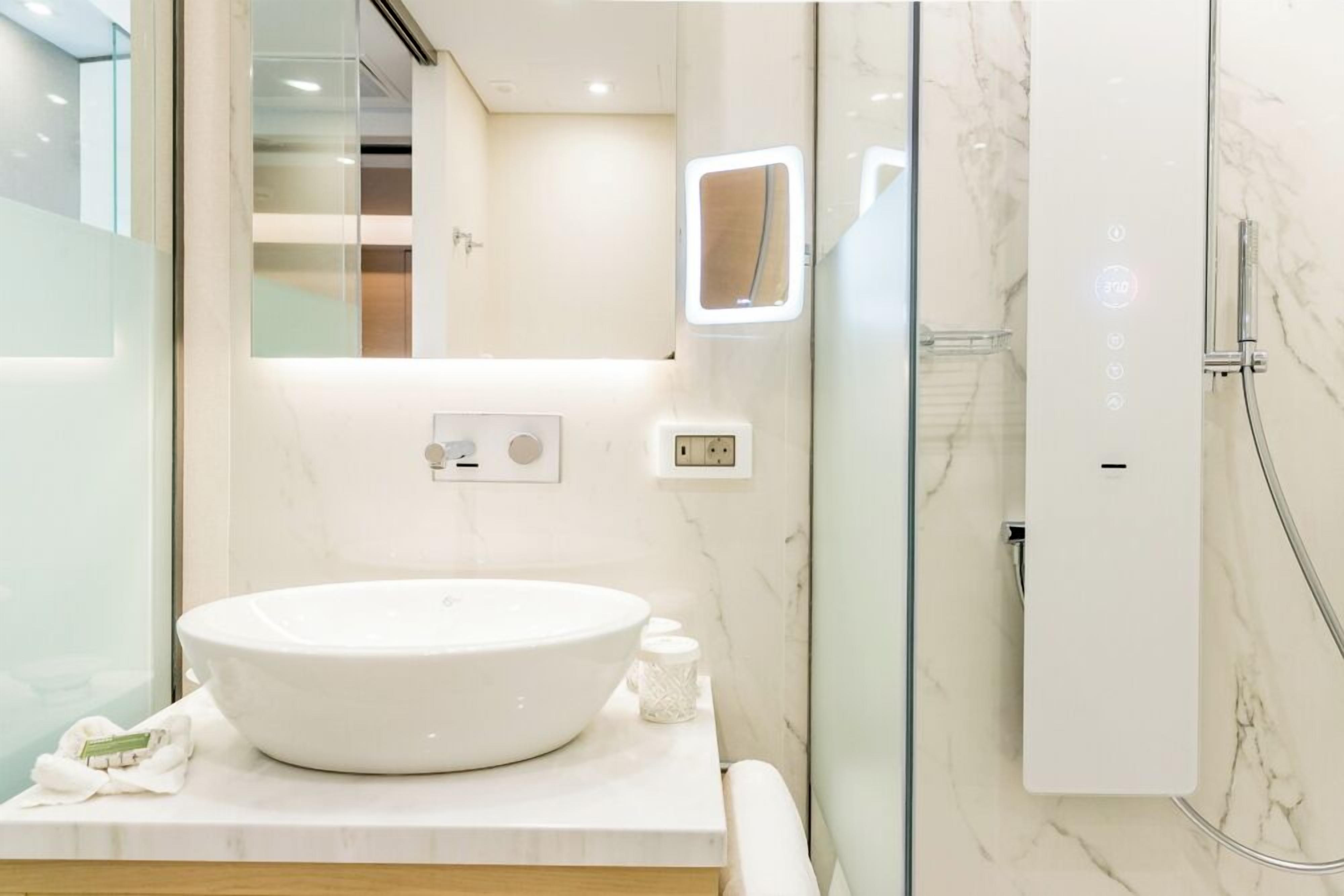 A modern bathroom with a large white sink, a glass shower enclosure, and a marble-tiled wall.
