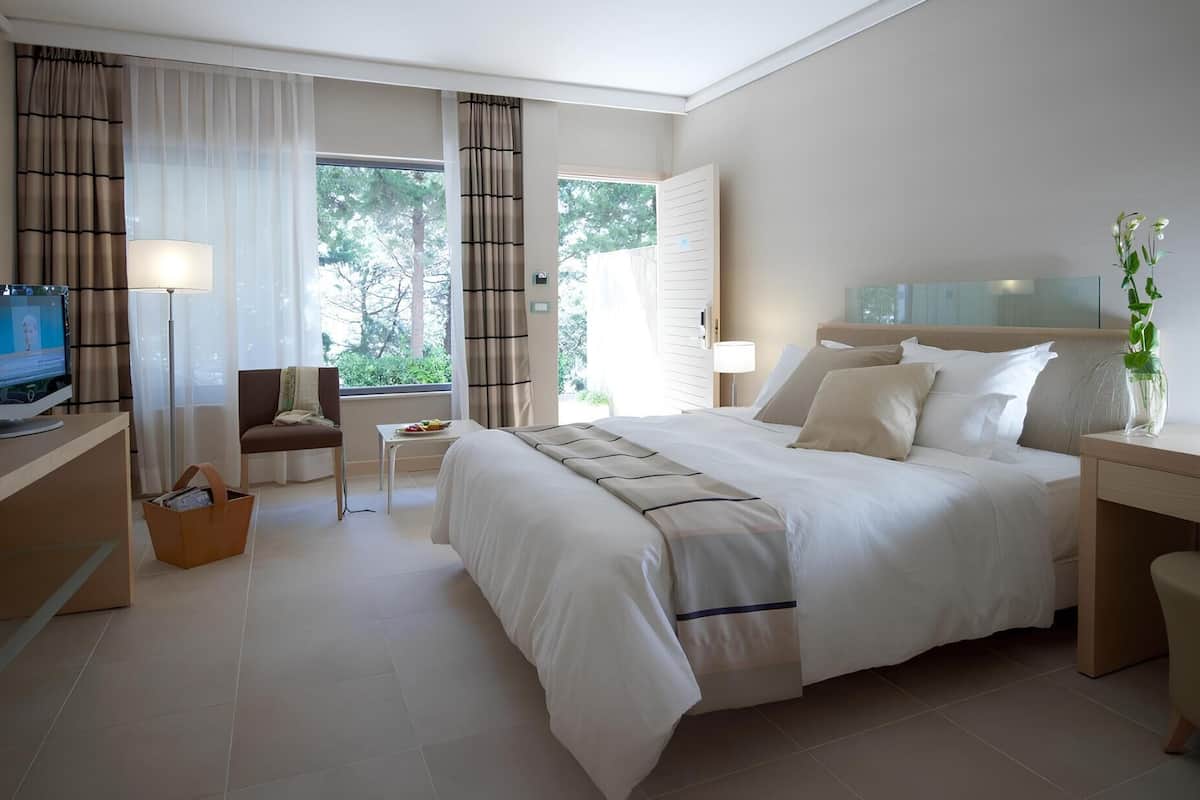 A hotel room with a bed, a desk, a chair, a TV, and a window with curtains.