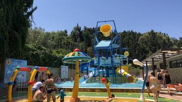 A water play area with slides and splash pads, surrounded by trees and a building with a modern design.