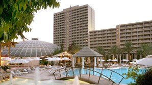 A hotel pool area with a bridge, lounge chairs, umbrellas, and a large building in the background. - Rodos Palace Hotel (Rhodes)