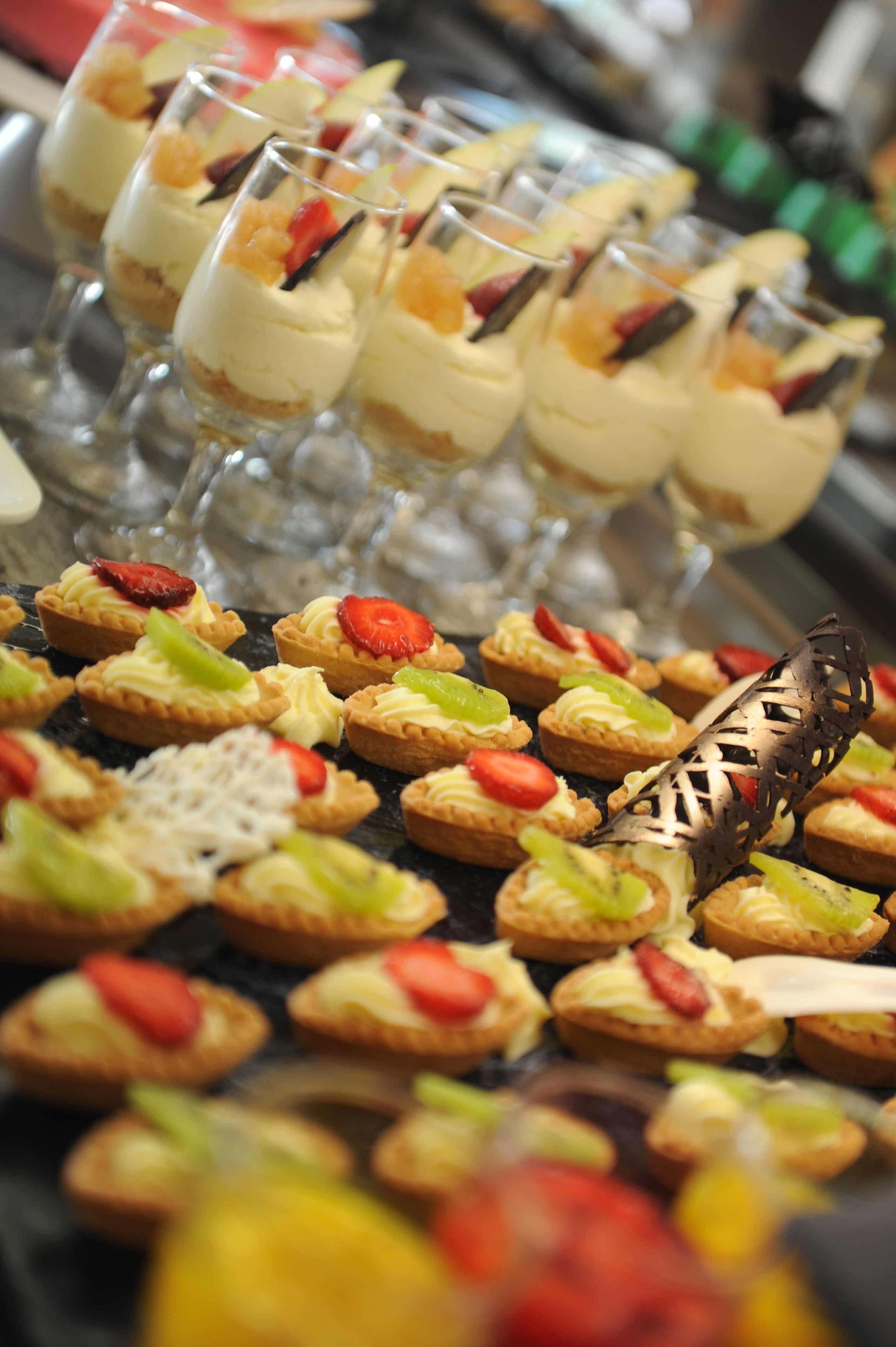Diversas sobremesas, incluindo mini tortas e parfaits, dispostas numa bandeja.