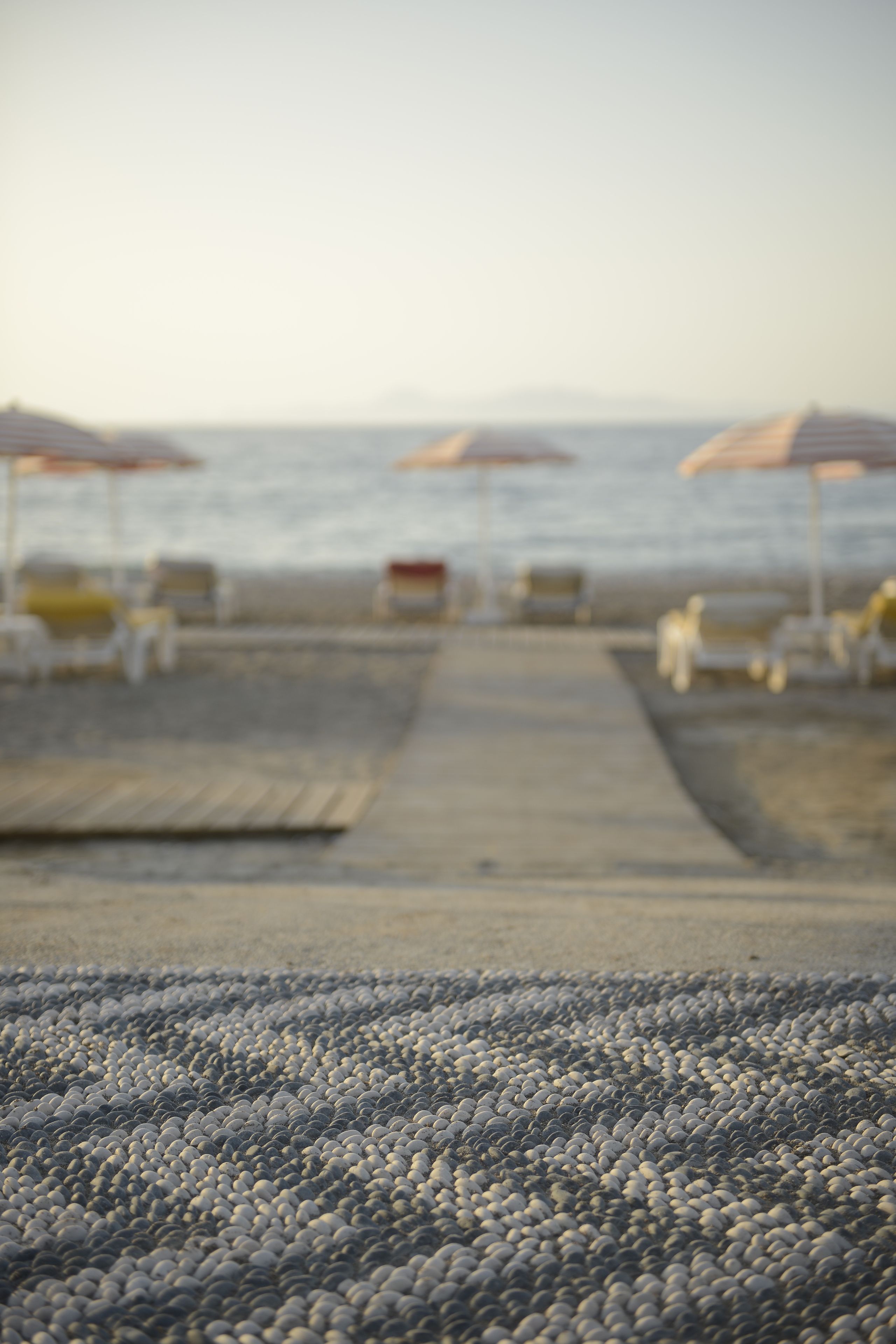 A pebble beach with umbrellas and lounge chairs.