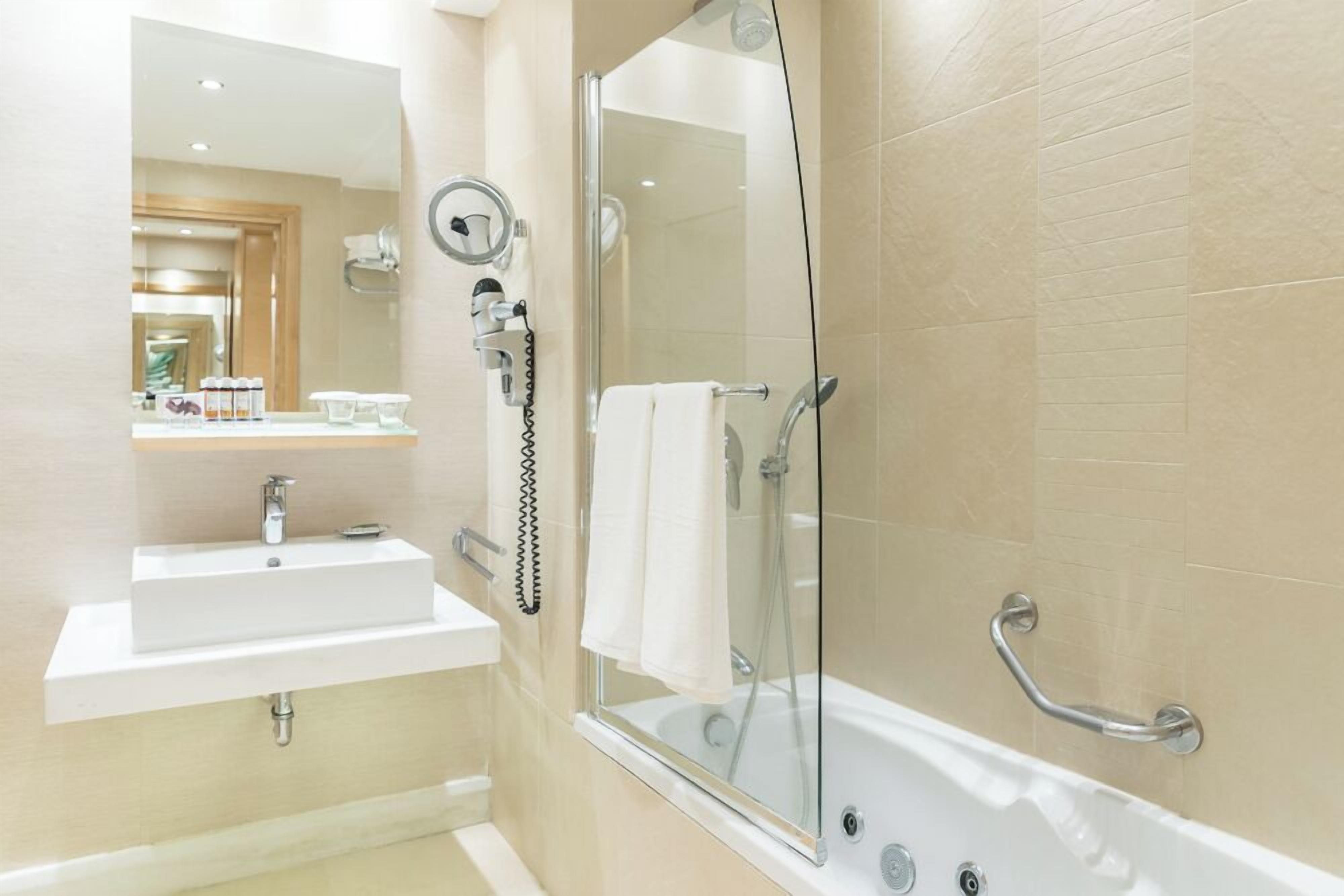 Un bagno con lavandino, specchio e cabina doccia in vetro dotata di maniglioni.