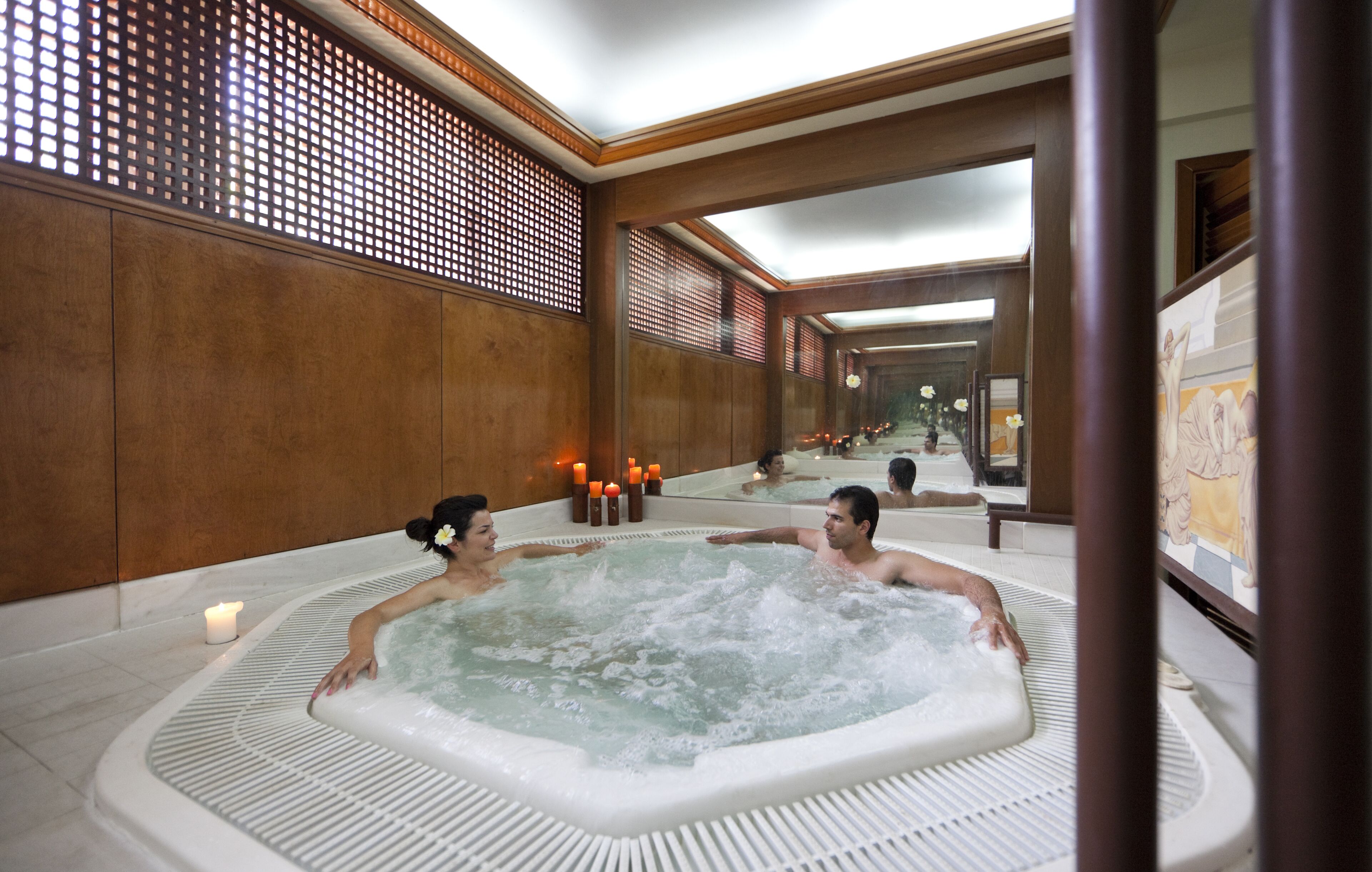 A spa area with a large hot tub, wooden paneling, and candles.