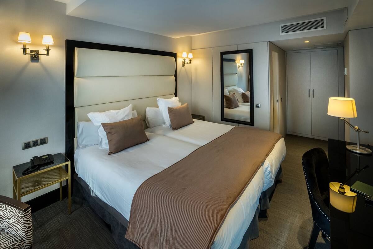 A hotel room with a large bed, bedside tables, a desk, and a mirror.