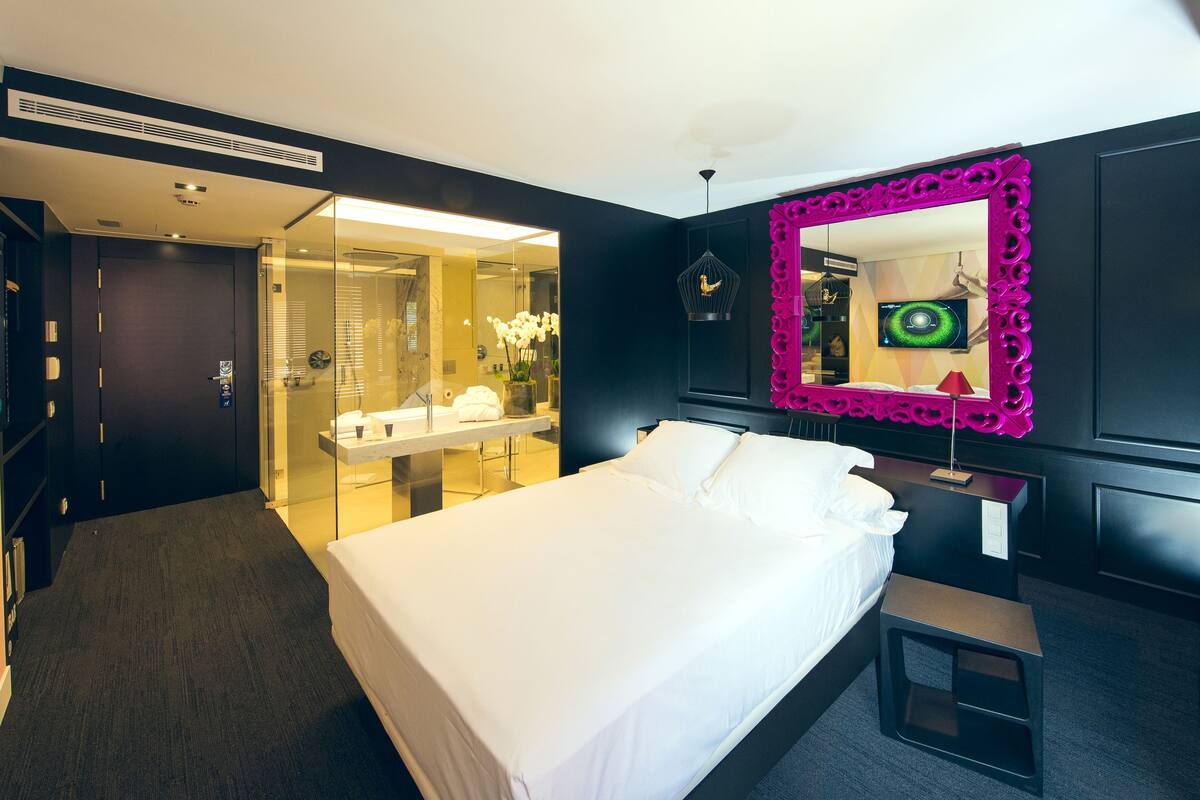 A modern hotel room with a large bed, a vanity with a mirror, and a walk-in closet.