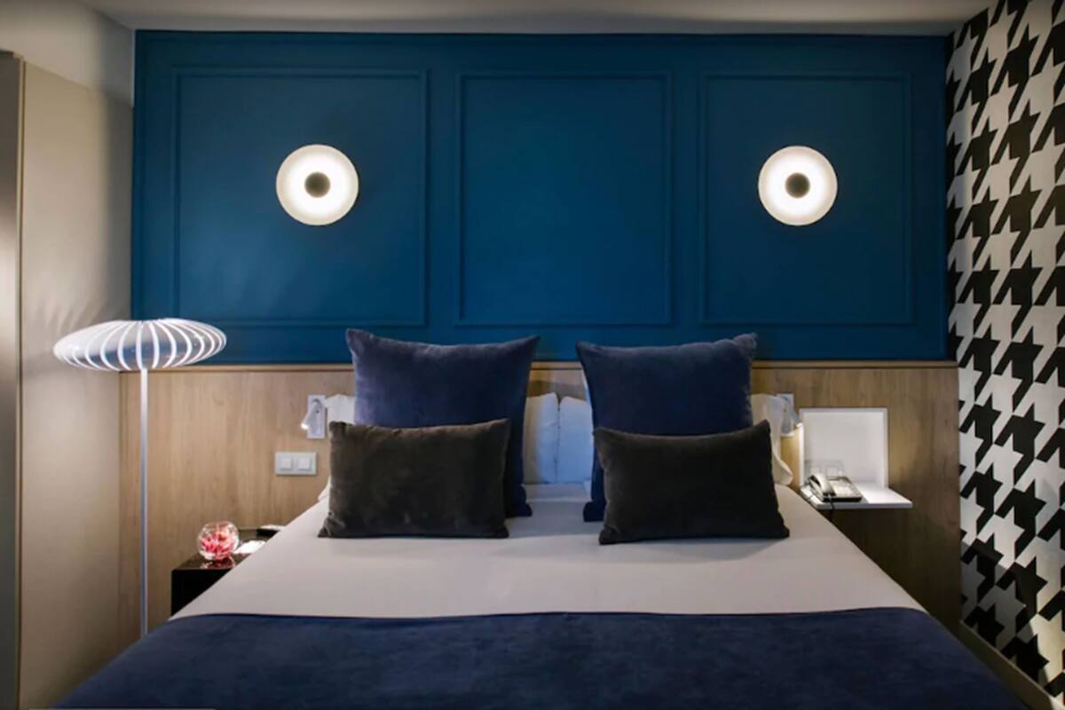 A hotel room with a large bed, two wall-mounted lights, a bedside table with a lamp, and a patterned wall.