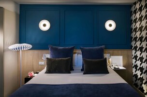 Camera d'albergo con un letto grande, due luci fissate al muro, un comodino con una lampada e una parete decorata.