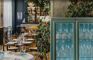 Un restaurante con mesas preparadas para comer, una zona de bar con botellas, y una pared decorativa con plantas.