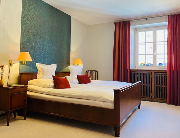 A neatly made bed with white and red pillows, a wooden headboard, and two bedside lamps.