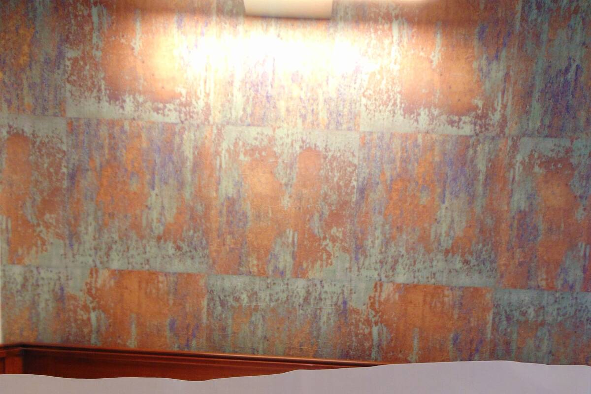 A pillow with the text "Oberkirch" on it, placed on a bed with a textured wall in the background.