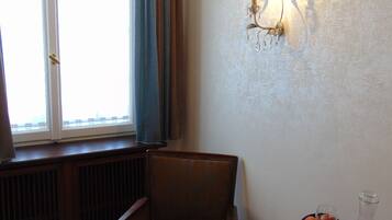 A room with a window, a radiator, a chair, a table with a book, a glass, and a bottle.
