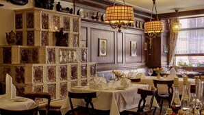 Un comedor con mesas dispuestas para el servicio, una araña y una pared de azulejos decorativos.