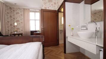 A hotel room with a wooden bed, a bathroom with a white sink and mirror, and a door leading to another room.
