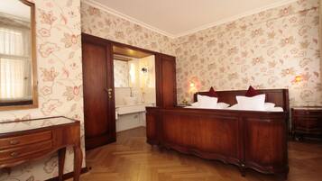 Ein Schlafzimmer mit einem Holzbett, einem Schminktisch, einem Spiegel und einem durch eine geöffnete Tür einsehbaren Badezimmer.