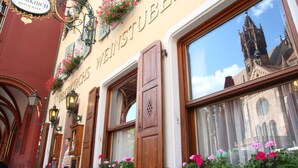Exterior de un hotel con un letrero que dice "Hotel Oberkirch Restaurant", contraventanas de madera, jardineras con flores y vista a una torre de iglesia.