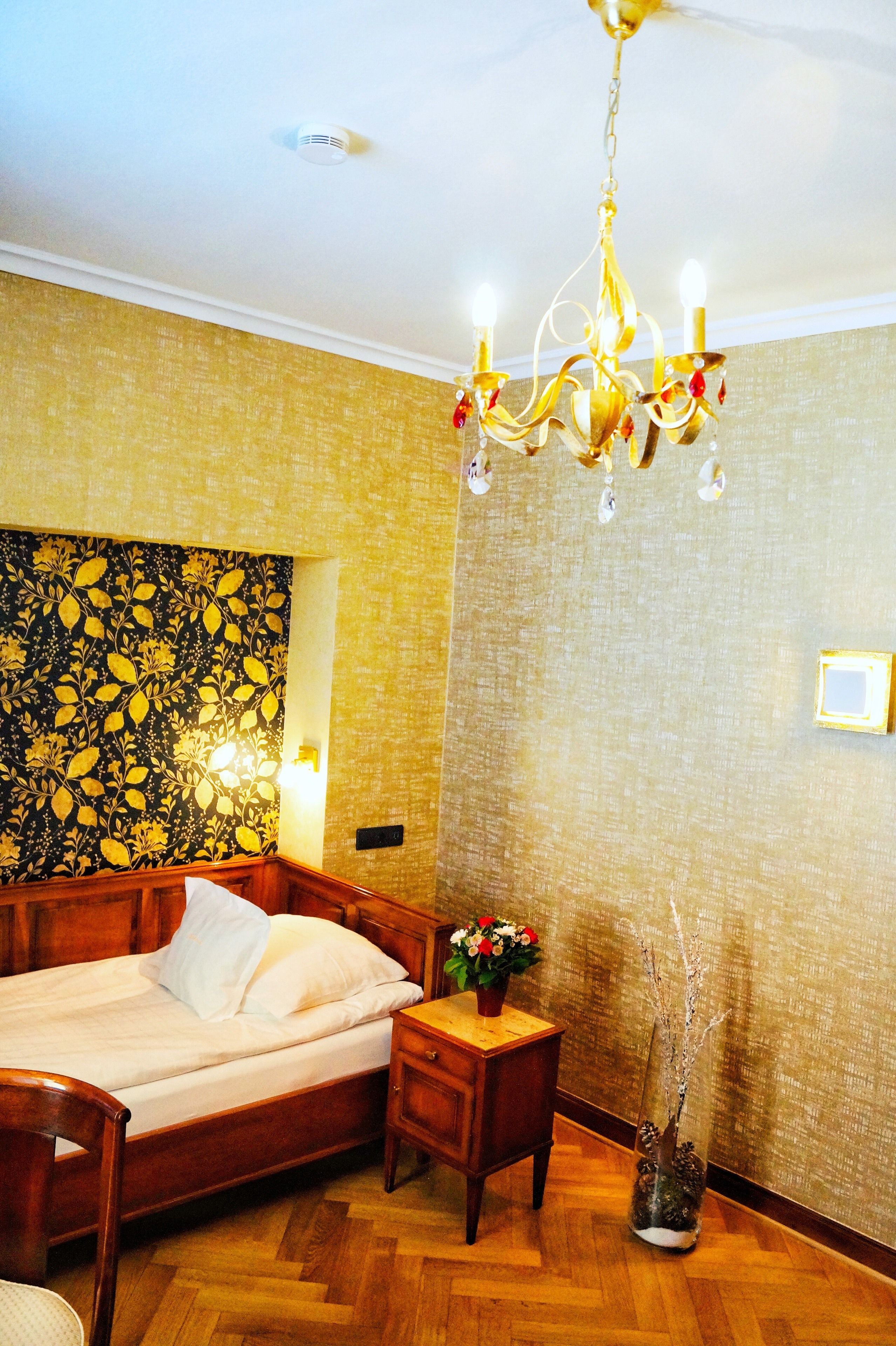 A bedroom with a wooden bed, a nightstand, a chandelier, and a floral wallpaper.