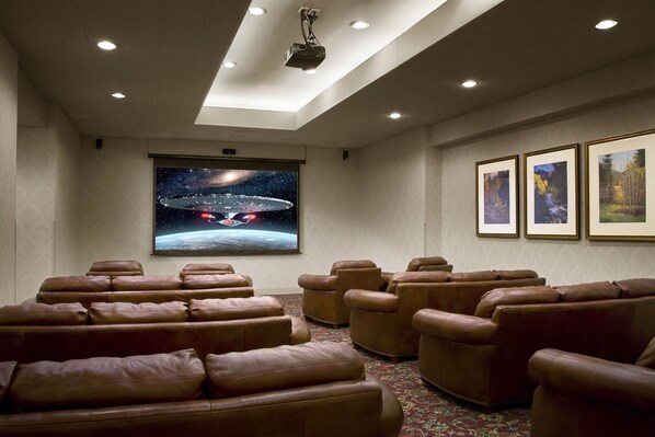 A home theater with leather reclining seats, a large screen, and framed pictures on the wall.