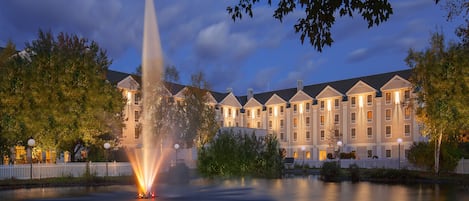 A hotel with a fountain in the courtyard, surrounded by trees and a white picket fence.