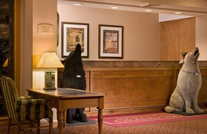 A lobby with two large dogs, a wooden reception desk, a lamp, and two framed artworks on the wall.