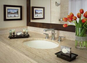 A bathroom with a marble sink, three faucets, framed pictures on the wall, and a vase with tulips.