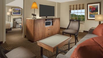 Une chambre d’hôtel équipée d’un téléviseur à écran plat, d’un meuble en bois contenant un four à micro-ondes, d’un canapé, d’une chaise et d’une petite table.